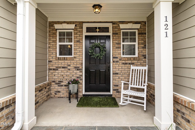 doorway to property featuring covered porch and brick siding