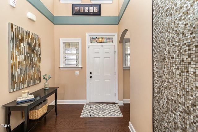 foyer with arched walkways, dark wood-style flooring, a towering ceiling, and baseboards