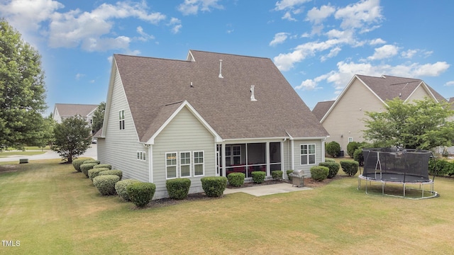 rear view of house with a trampoline, a sunroom, roof with shingles, and a yard