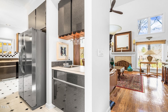 kitchen with a sink, light wood-style floors, stainless steel refrigerator with ice dispenser, a brick fireplace, and dishwasher