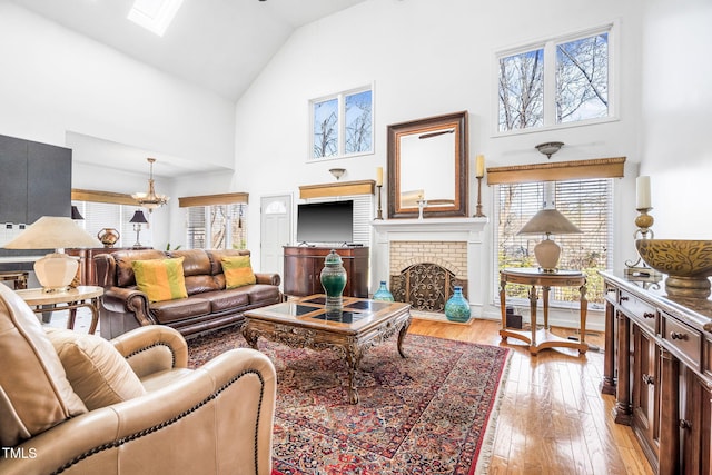 living room with a skylight, light wood-style flooring, a fireplace, and high vaulted ceiling