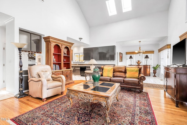 living area with a skylight, light wood-style flooring, high vaulted ceiling, and a notable chandelier