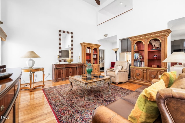 living room featuring ceiling fan, a towering ceiling, and light wood-style flooring