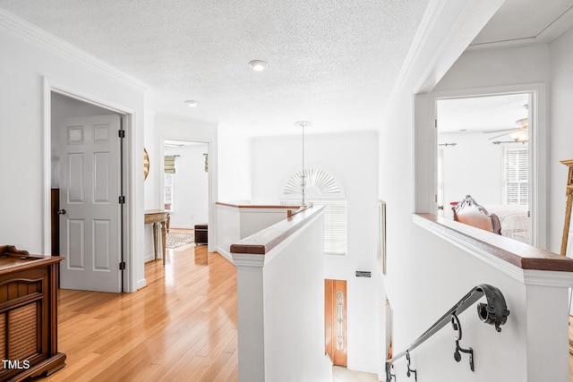 hallway featuring light wood finished floors, ornamental molding, a textured ceiling, and an upstairs landing