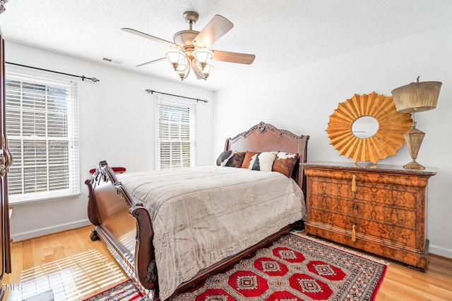 bedroom with a textured ceiling, wood finished floors, a ceiling fan, visible vents, and baseboards