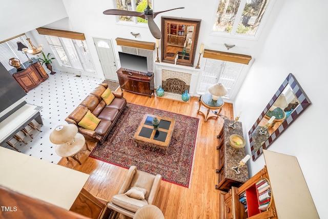 living room with a towering ceiling, a brick fireplace, plenty of natural light, and wood finished floors