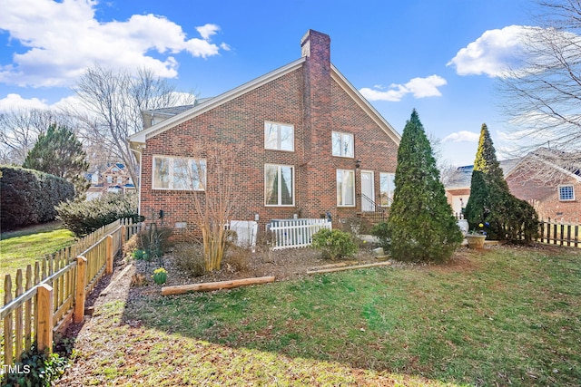 back of house with a yard, brick siding, fence, and a chimney