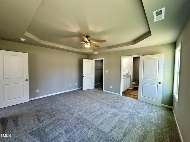 unfurnished bedroom with baseboards, visible vents, a spacious closet, a raised ceiling, and dark carpet