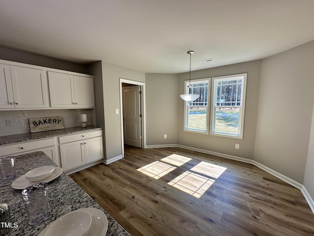 unfurnished dining area featuring dark wood-style floors, visible vents, and baseboards