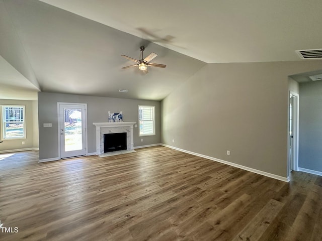 unfurnished living room featuring a high end fireplace, visible vents, baseboards, vaulted ceiling, and wood finished floors