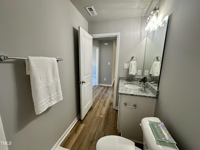 half bathroom with visible vents, toilet, wood finished floors, baseboards, and vanity