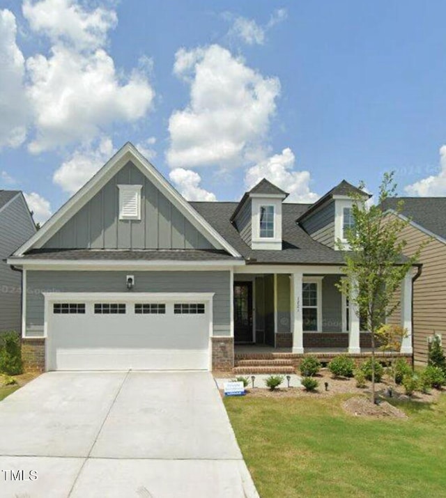 view of front of house with brick siding, a porch, a garage, driveway, and a front lawn