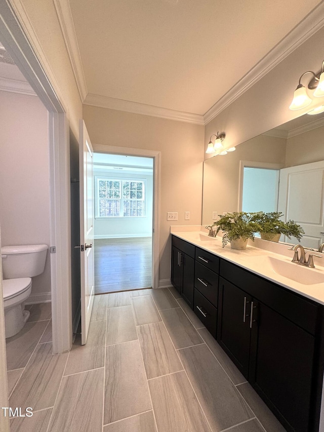 bathroom with toilet, double vanity, ornamental molding, and a sink