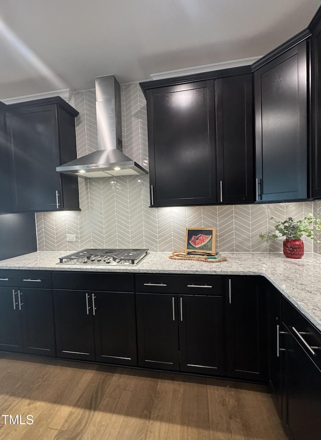 kitchen with decorative backsplash, dark cabinets, wall chimney range hood, and light wood finished floors