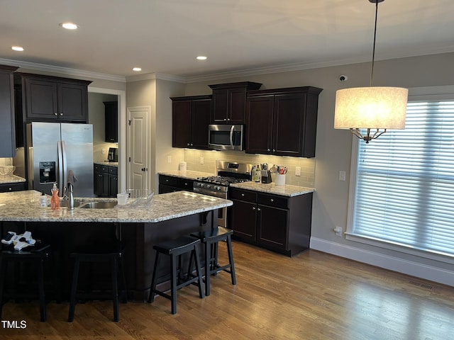 kitchen featuring wood finished floors, a sink, appliances with stainless steel finishes, decorative backsplash, and crown molding