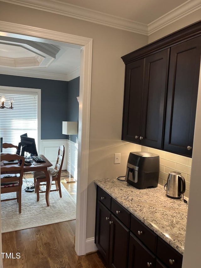 kitchen featuring a wainscoted wall, ornamental molding, dark wood finished floors, and light stone counters