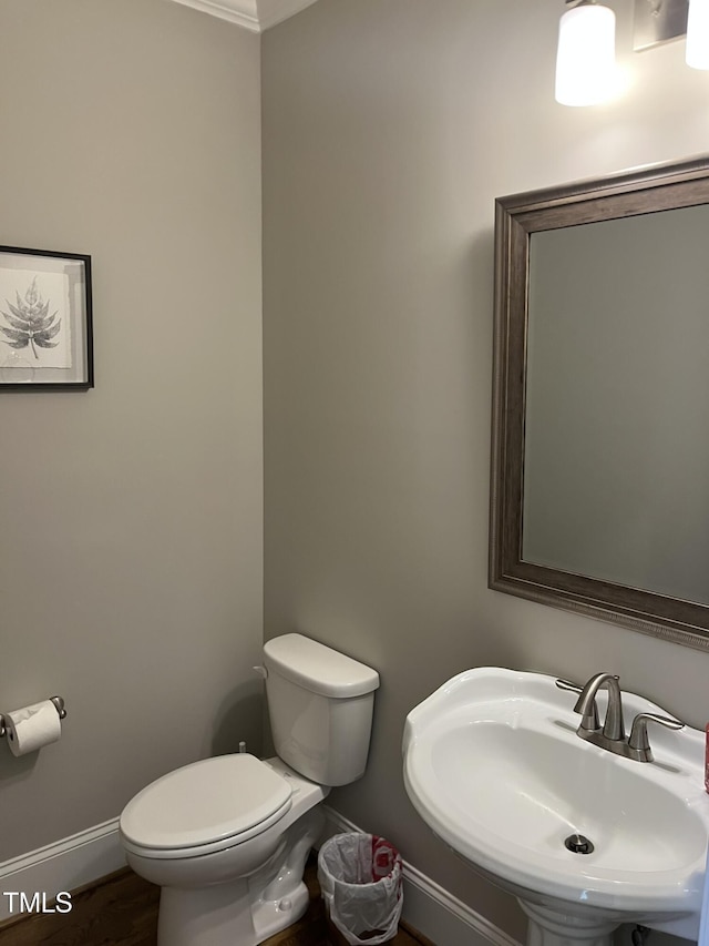 half bathroom featuring wood finished floors, a sink, toilet, and baseboards