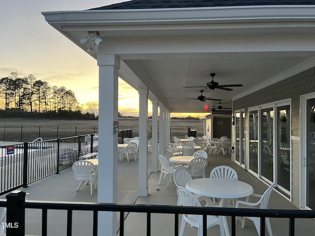 patio terrace at dusk featuring ceiling fan, outdoor dining space, and fence