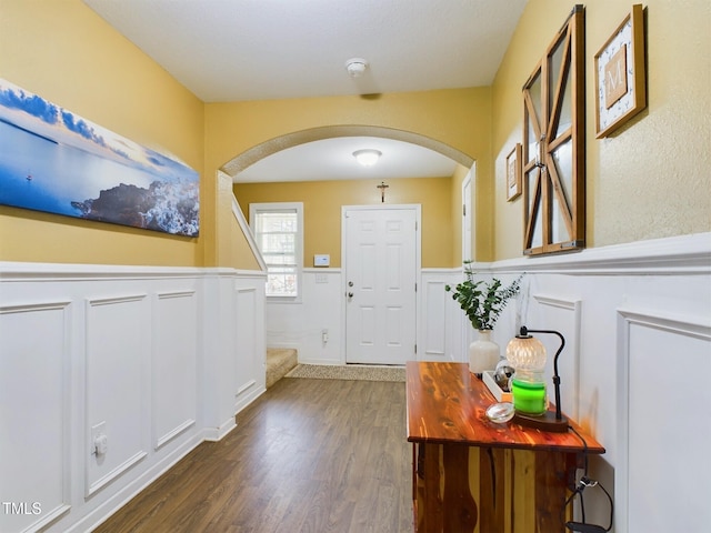 doorway to outside featuring arched walkways, dark wood-style flooring, and wainscoting