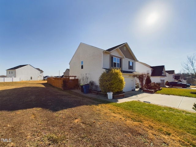 view of home's exterior with a yard, concrete driveway, fence, a garage, and a residential view