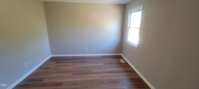 spare room featuring dark wood-style flooring, visible vents, and baseboards