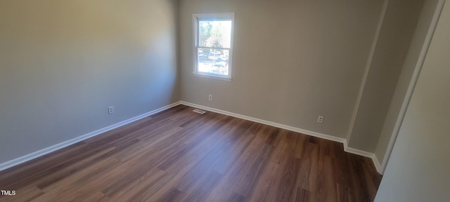 empty room featuring dark wood-style flooring, visible vents, and baseboards