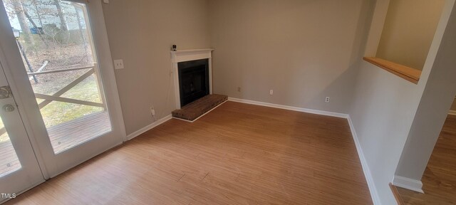 unfurnished living room featuring a brick fireplace, wood finished floors, and baseboards