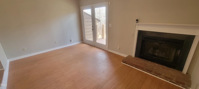 unfurnished living room featuring a fireplace with raised hearth, wood finished floors, and baseboards