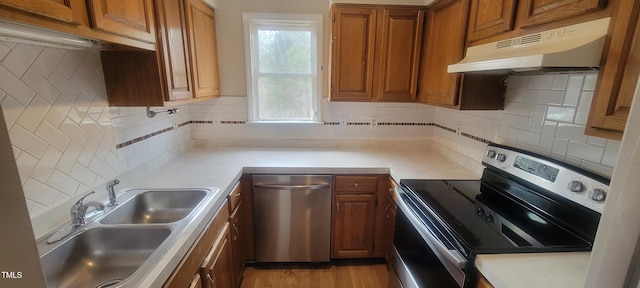 kitchen featuring brown cabinets, stainless steel appliances, light countertops, under cabinet range hood, and a sink