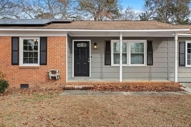 property entrance with roof with shingles, crawl space, covered porch, roof mounted solar panels, and brick siding