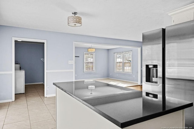 kitchen featuring light tile patterned floors, baseboards, stainless steel fridge with ice dispenser, dark countertops, and pendant lighting