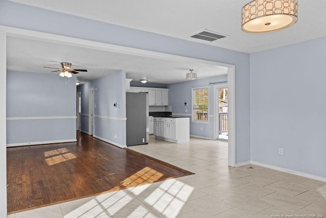 unfurnished living room with ceiling fan, light tile patterned flooring, visible vents, and baseboards