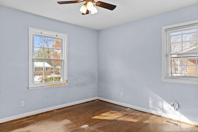 spare room featuring plenty of natural light, visible vents, baseboards, and wood finished floors