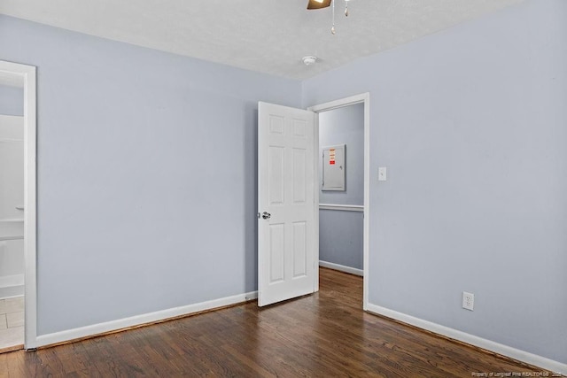 empty room with electric panel, baseboards, dark wood finished floors, and a ceiling fan