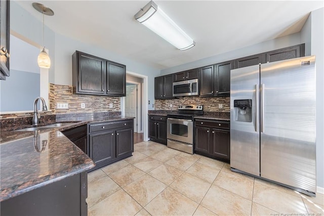 kitchen featuring dark stone counters, appliances with stainless steel finishes, decorative light fixtures, a sink, and backsplash