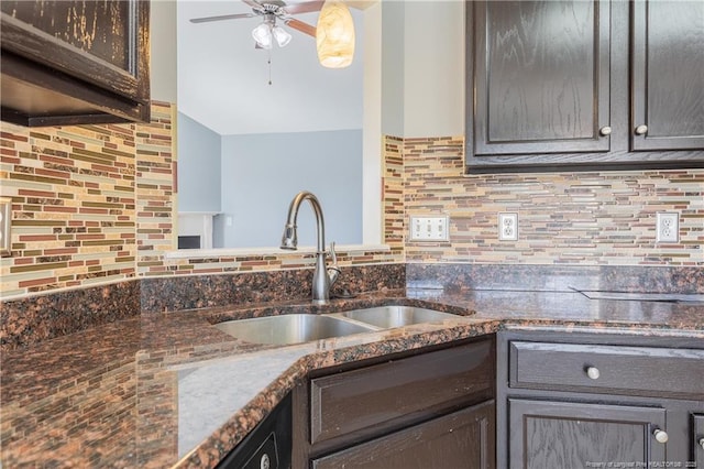 kitchen with dark brown cabinetry, decorative backsplash, ceiling fan, dark stone countertops, and a sink