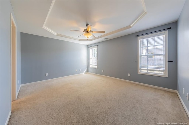 unfurnished room featuring a raised ceiling, light colored carpet, visible vents, a ceiling fan, and baseboards