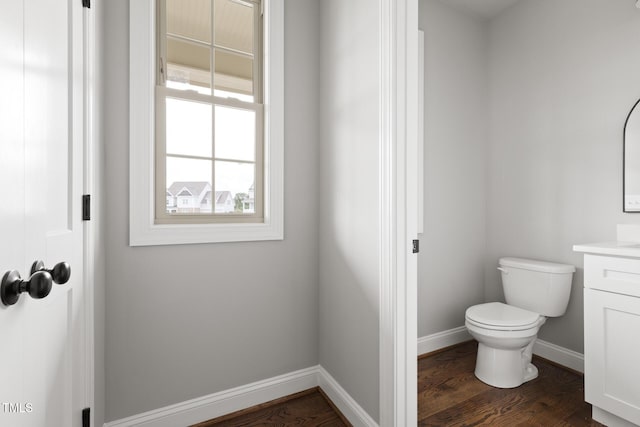 half bathroom with toilet, baseboards, wood finished floors, and vanity