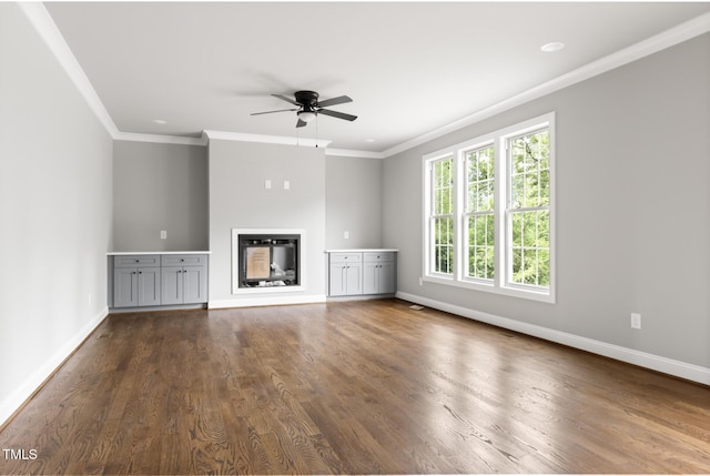 unfurnished living room featuring dark wood-style flooring, a ceiling fan, baseboards, a glass covered fireplace, and crown molding