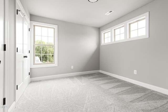 unfurnished room with a wealth of natural light, visible vents, light carpet, and baseboards