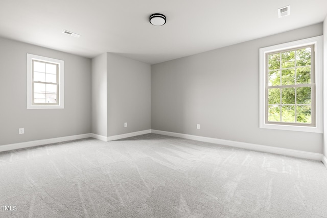 spare room featuring light colored carpet, visible vents, and baseboards