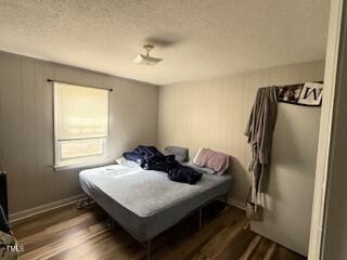 bedroom with dark wood-style floors, a textured ceiling, and baseboards