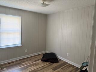 empty room featuring a textured ceiling, wood finished floors, and baseboards