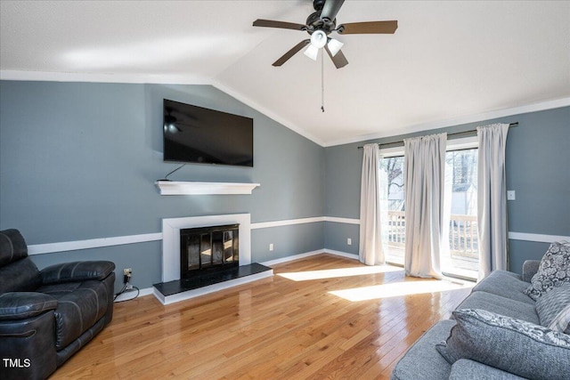 living area with hardwood / wood-style flooring, baseboards, vaulted ceiling, ornamental molding, and a glass covered fireplace