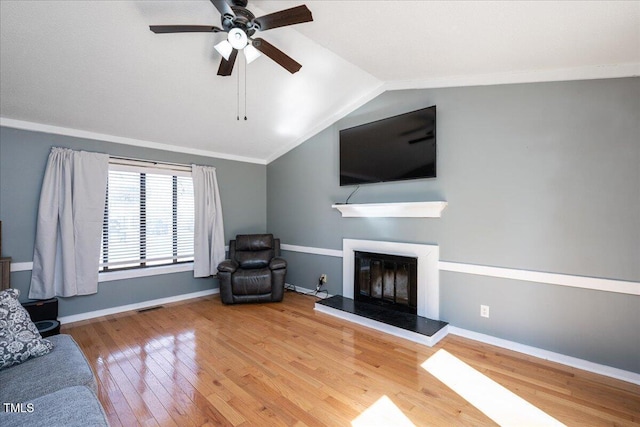 living room featuring baseboards, a glass covered fireplace, lofted ceiling, wood-type flooring, and crown molding