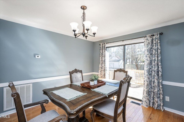 dining area featuring crown molding, visible vents, a textured ceiling, wood finished floors, and a chandelier