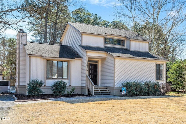 view of front of property with a shingled roof, a front yard, and a chimney