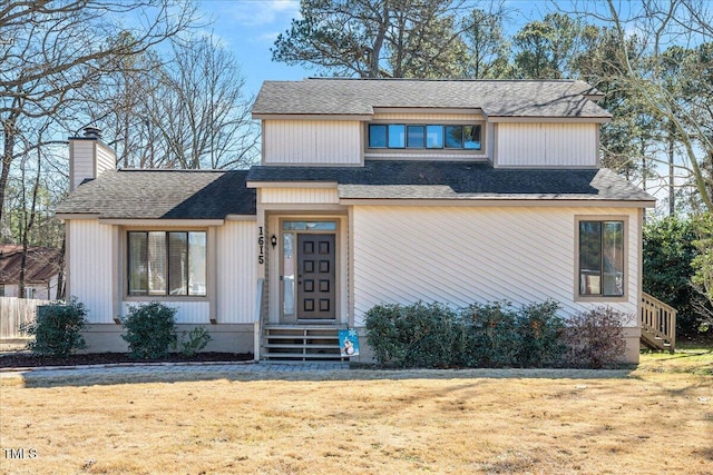 view of front facade with a shingled roof, a chimney, and a front yard