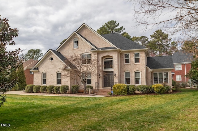 view of front of house featuring brick siding, roof with shingles, and a front yard