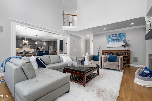 living area featuring baseboards, ornamental molding, wood finished floors, a high ceiling, and recessed lighting